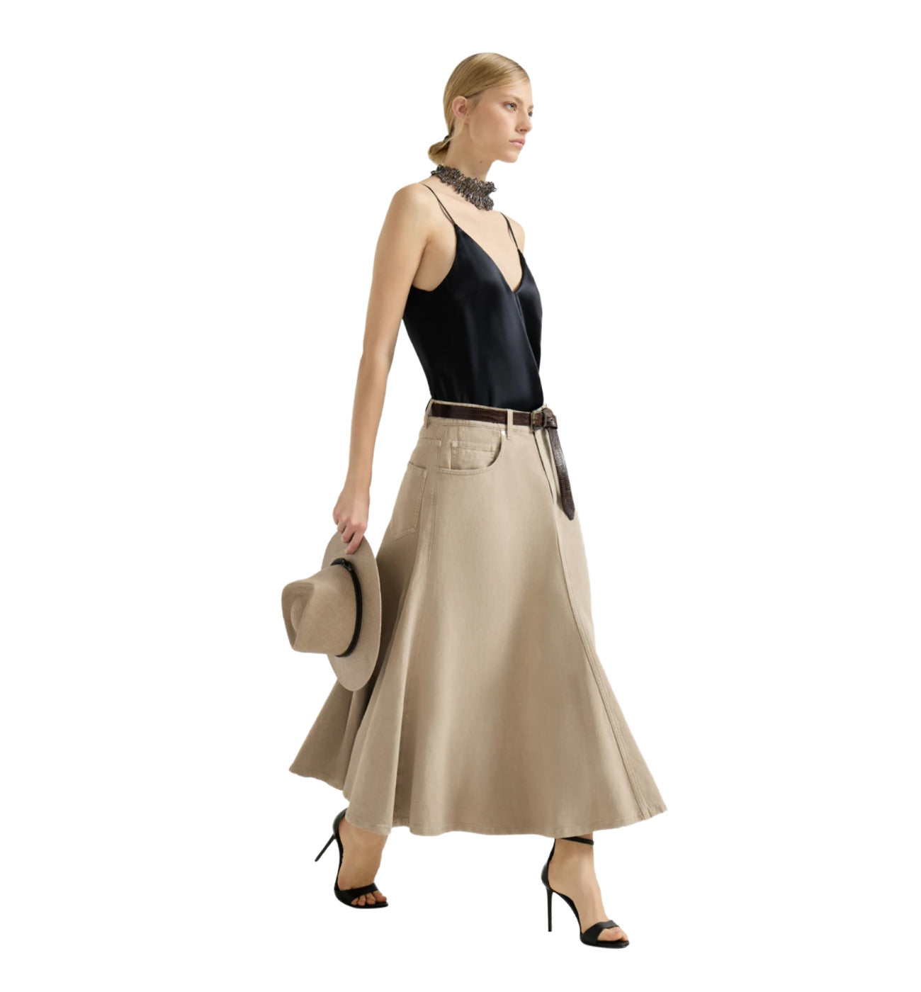 Woman wearing a black top and beige skirt holding a hat on a white background