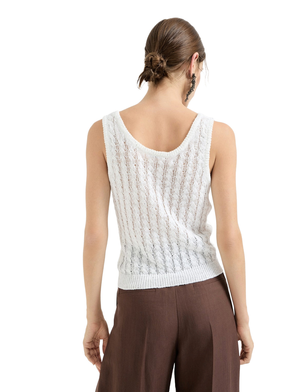 Woman wearing a white sleeveless knitted top and brown pants on a white background