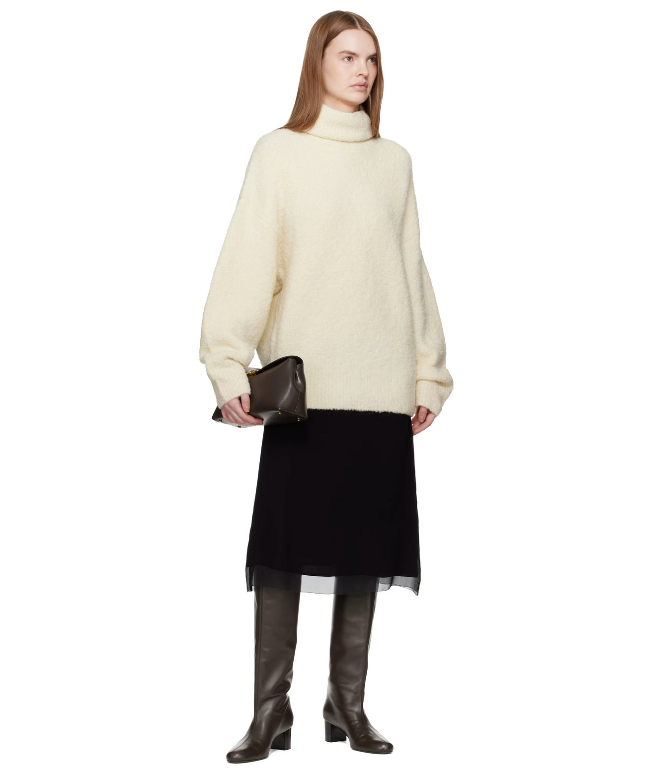 Person wearing a cream sweater, black skirt, and brown boots on a white background