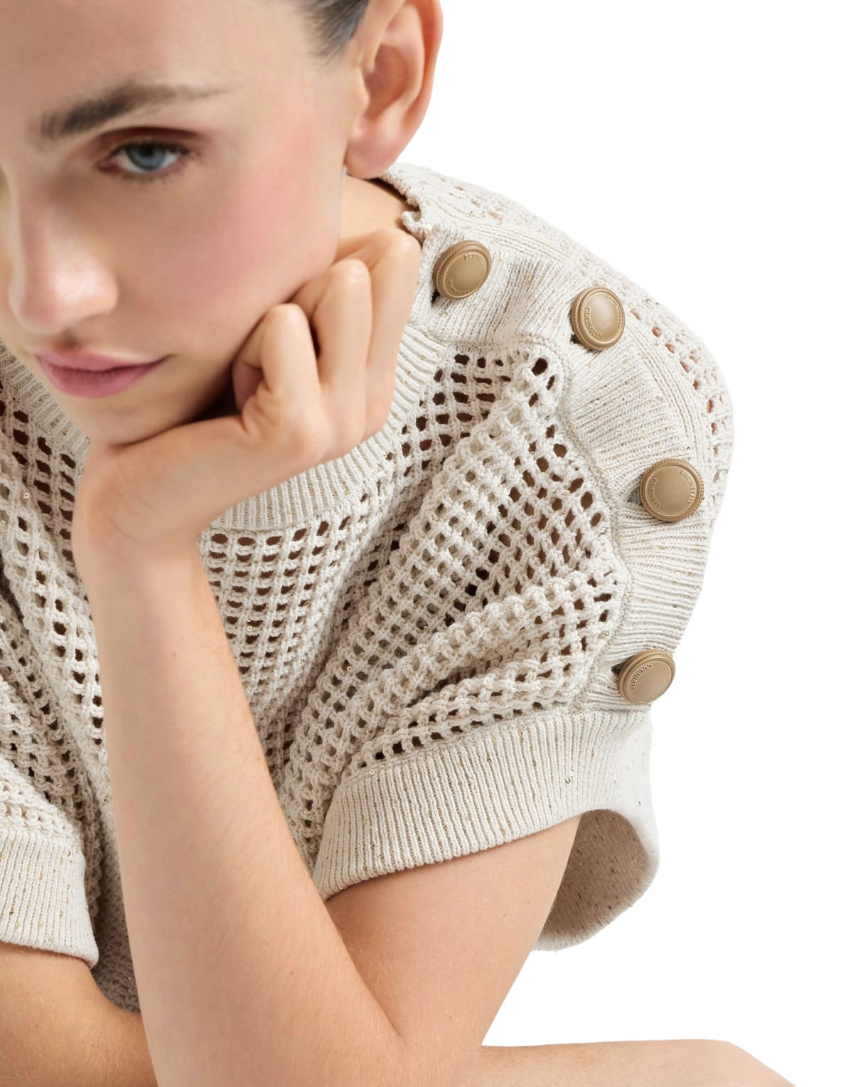 Woman wearing a beige knit top with button details on a white background