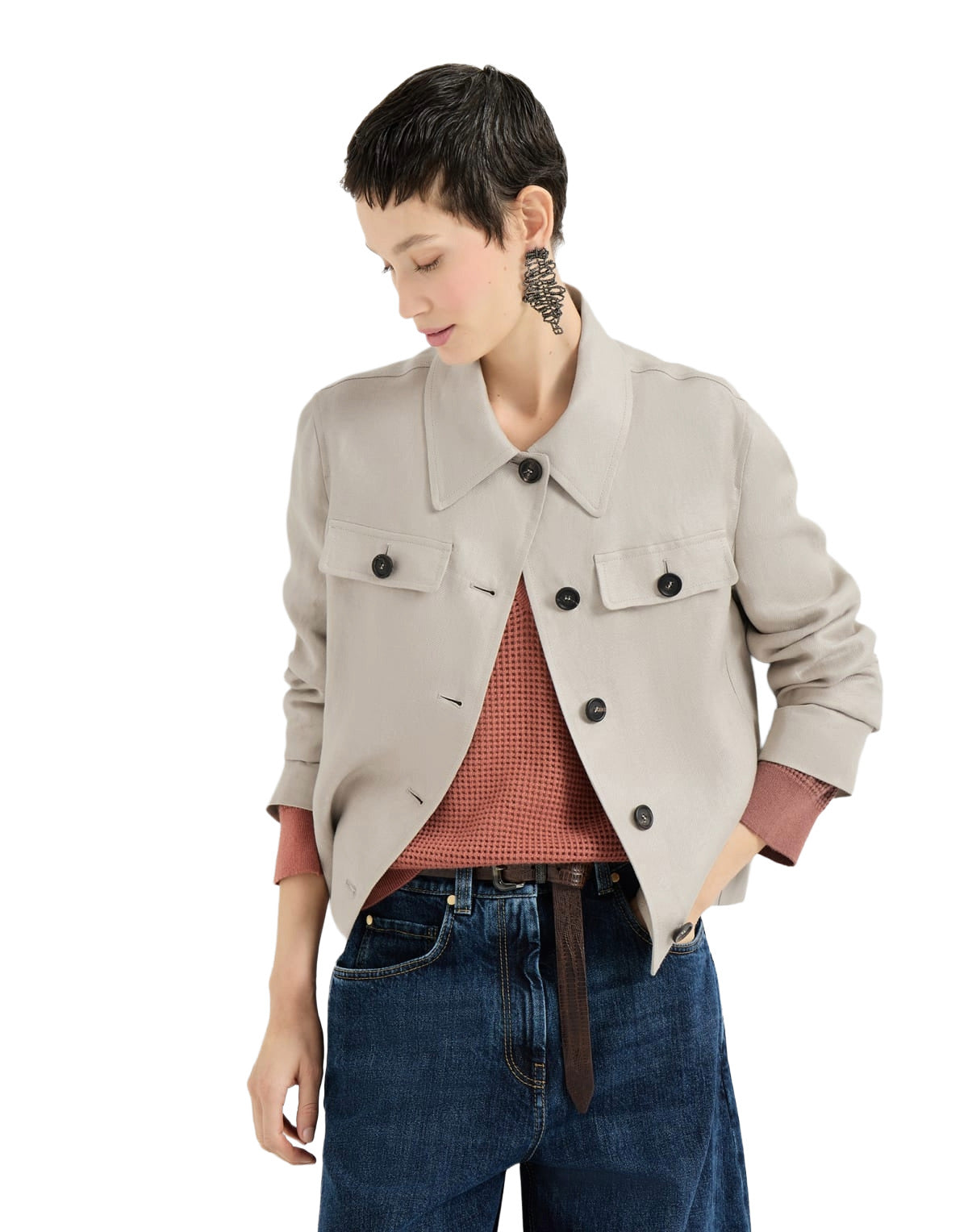 Woman wearing a beige jacket over a red sweater with blue jeans on a white background