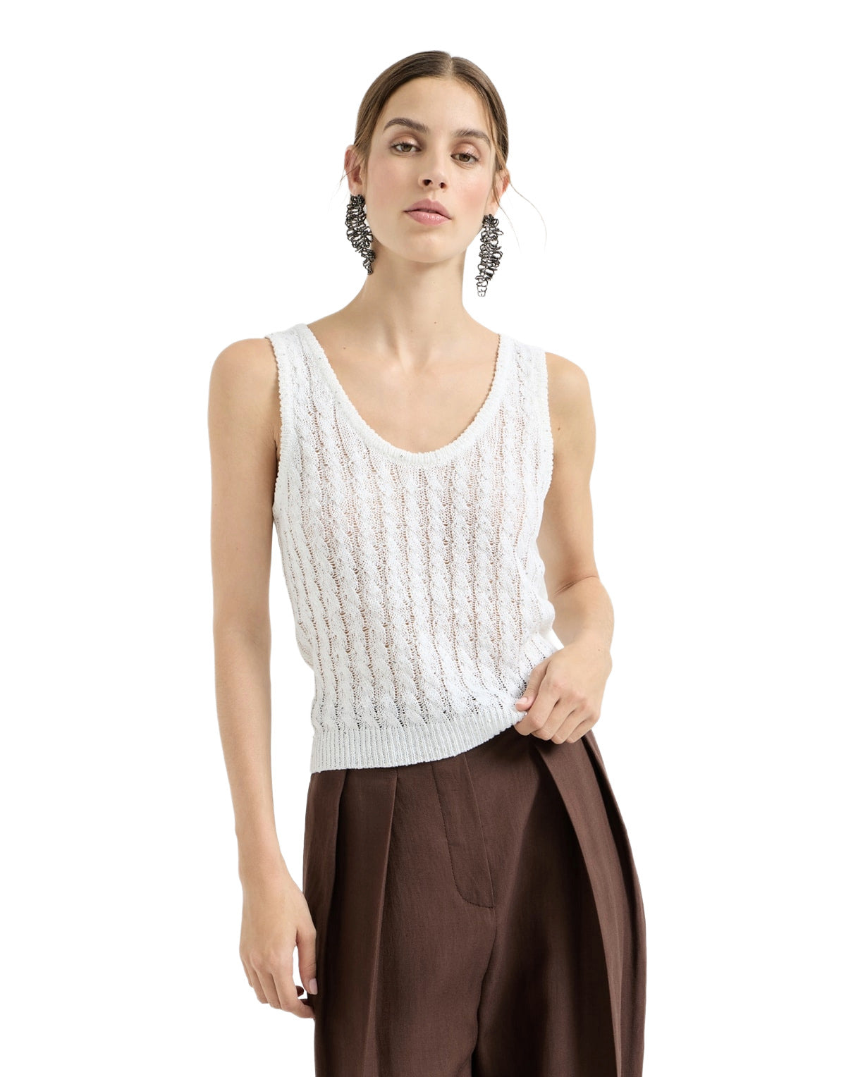 Woman wearing a white sleeveless knitted top and brown pants on a white background