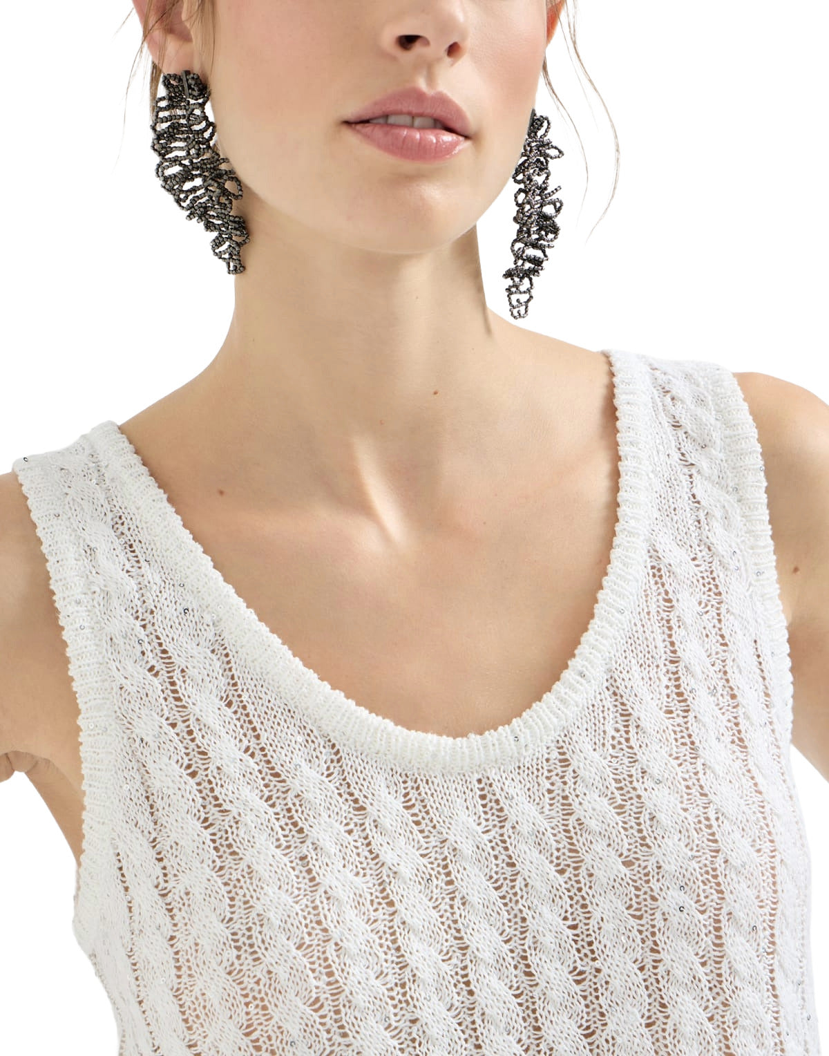 Woman wearing a white sleeveless top and large hoop earrings on a white background