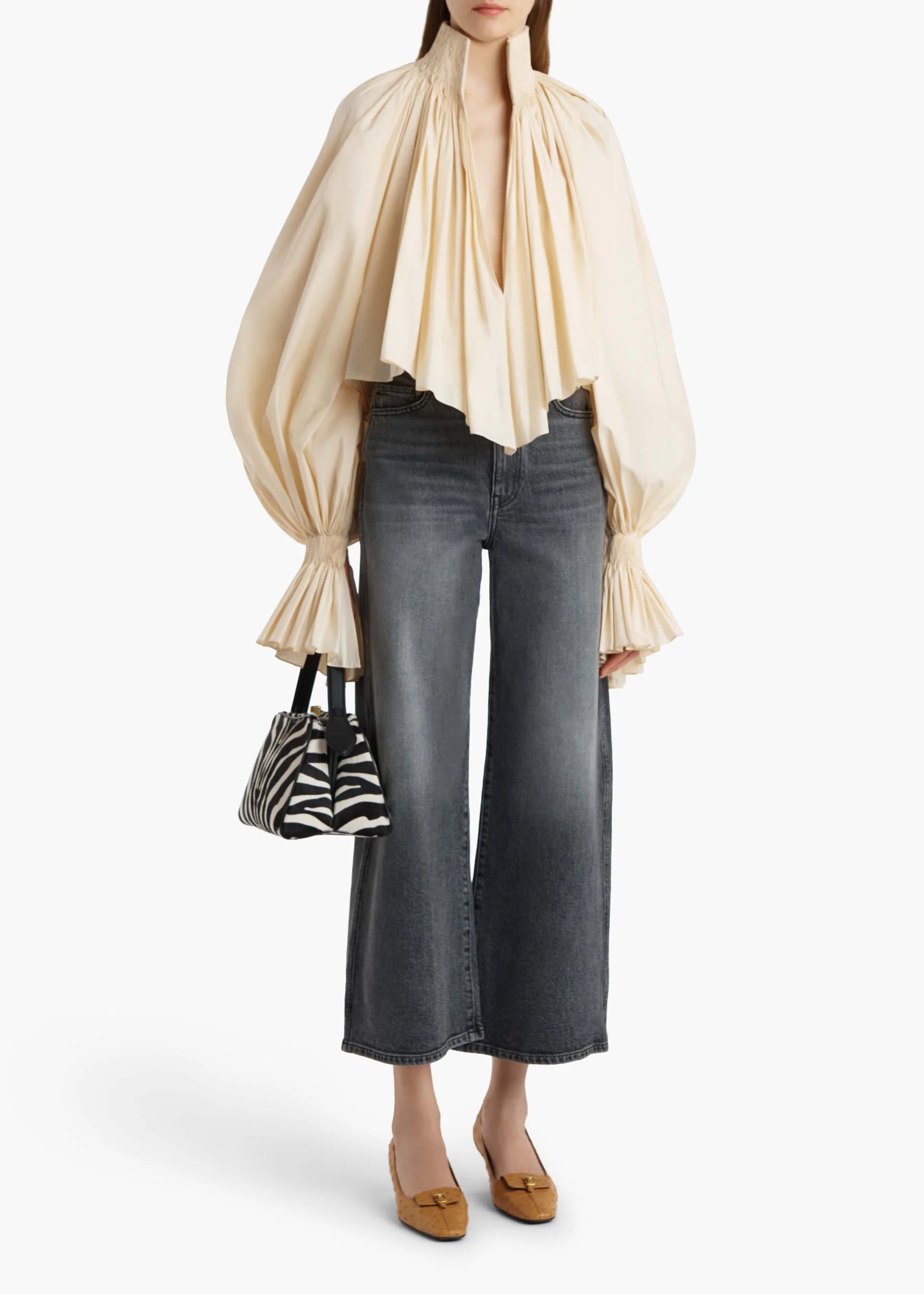 Model wearing black jeans with a beige top in front of a white backdrop.