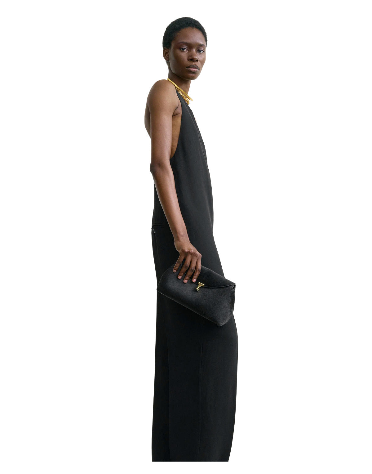 Woman in a black sleeveless dress holding a black clutch against a white background