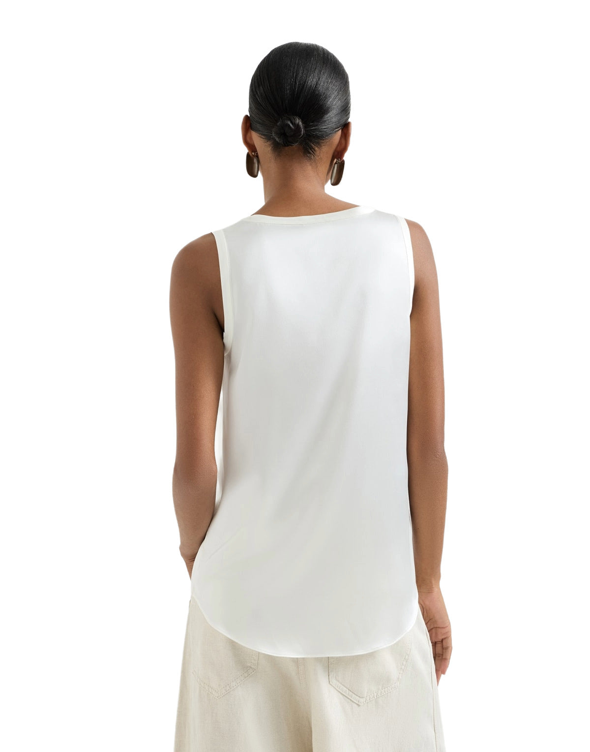 Woman wearing a white sleeveless top and light-colored pants on a white background